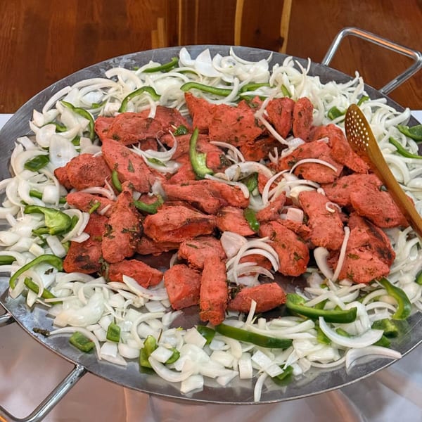 Red Indian chicken tikka pieces, white onions, and green bell peppers in a large metal pan.
