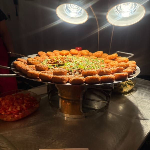 A large, round platter of golden-brown fried patties surrounds a center of saucy beans and herbs.