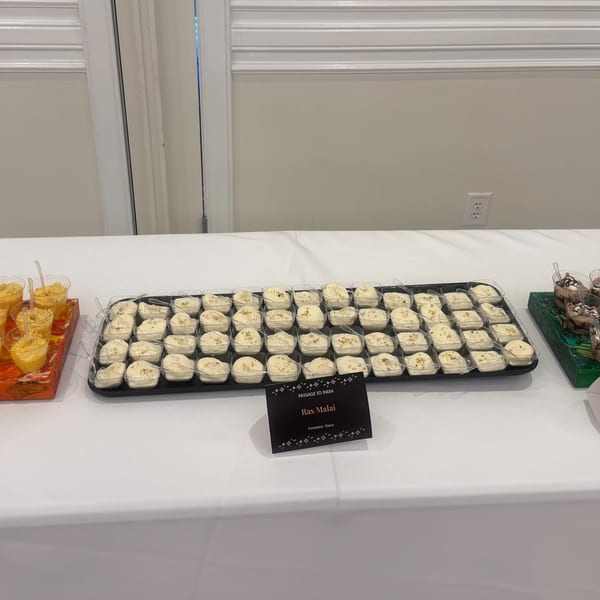 A buffet table with trays of Ras Malai and other desserts in small clear cups.