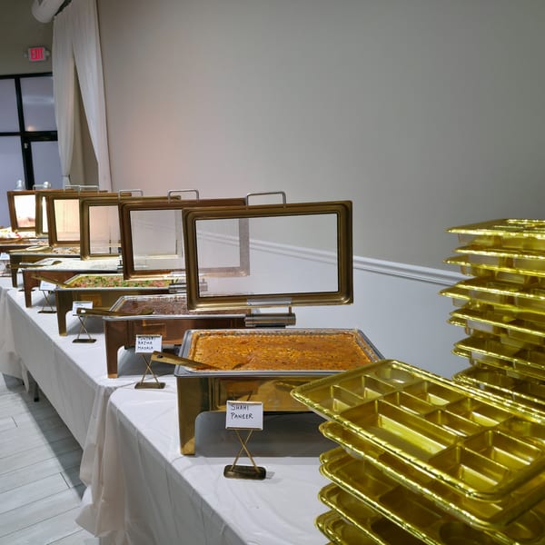 A buffet line of Indian food in golden chafing dishes with stacked golden serving trays.