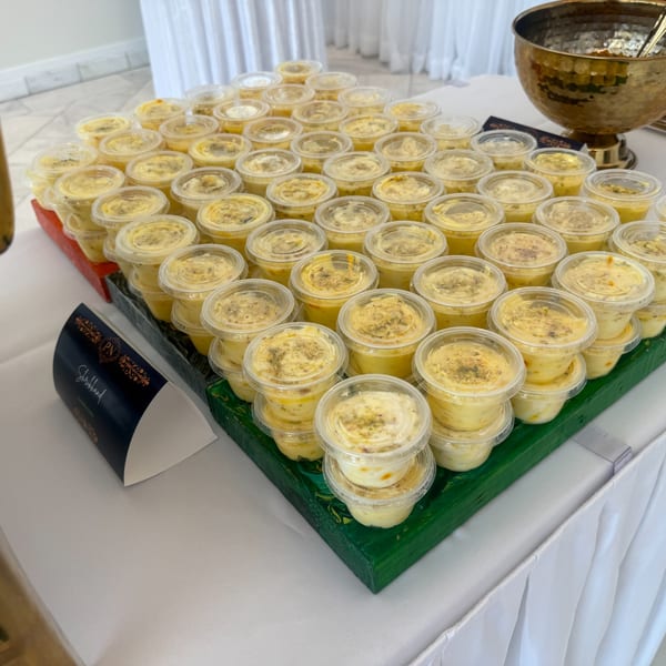 Numerous small, clear plastic cups of yellow shrikhand dessert with green garnish on a green tray.
