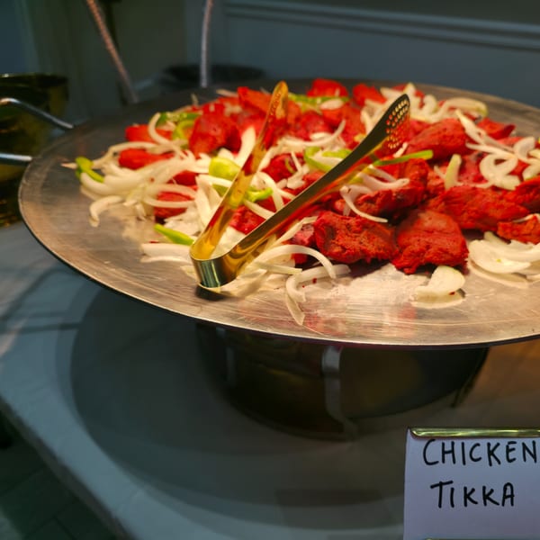 Chicken Tikka, a red Indian dish with onions and green peppers, on a silver platter.
