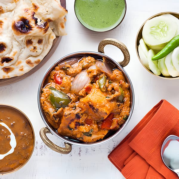 Overhead view of Indian chicken curry, naan, dal, green chutney, and cucumber salad on a white table.