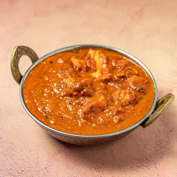 A metal bowl filled with Passage To India's vibrant orange Indian curry with chicken pieces.
