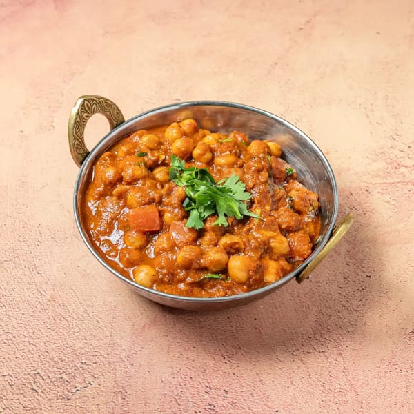 Passage To India's Chana Masala, a chickpea curry, garnished with fresh cilantro in a traditional copper bowl.