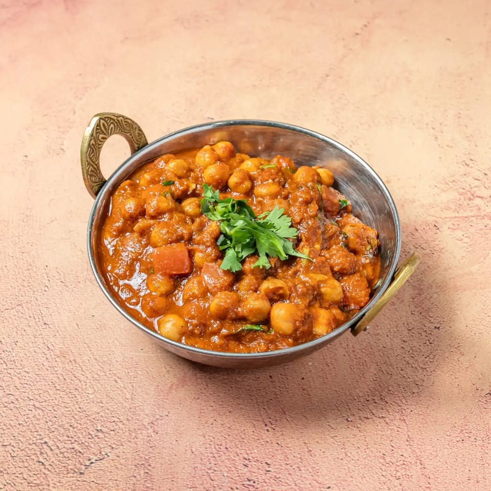 Passage To India's Chana Masala, a chickpea curry, garnished with fresh cilantro in a traditional copper bowl.