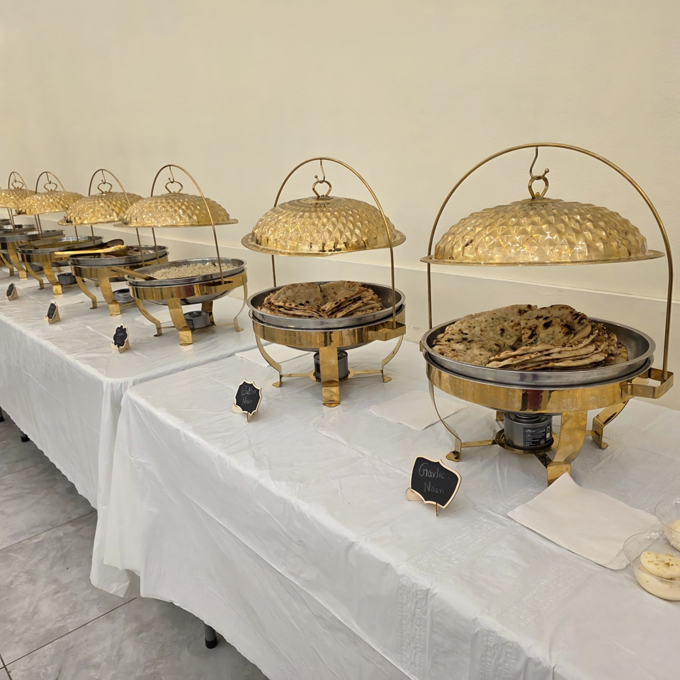 A buffet line of golden chafing dishes filled with Indian naan bread and rice.