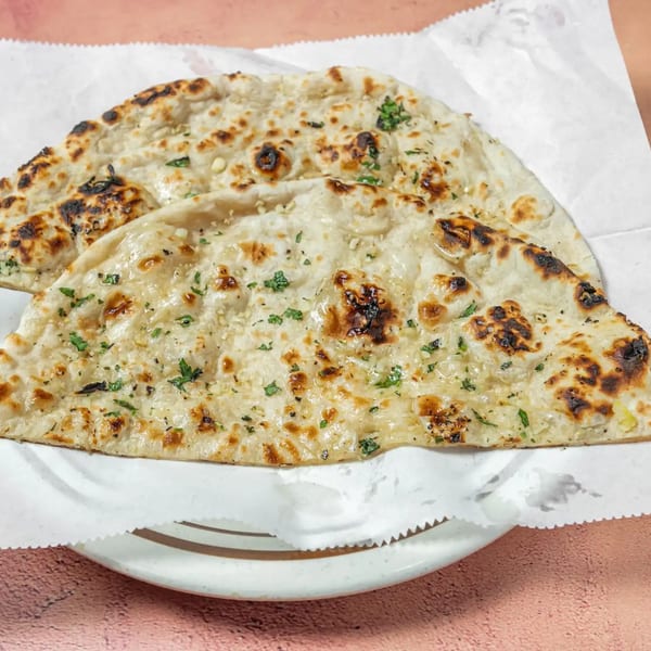 Two pieces of Passage To India's garlic naan, garnished with herbs, on a white plate.