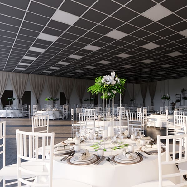 A large event hall with white round tables, chairs, and floral centerpieces under a checkered ceiling.