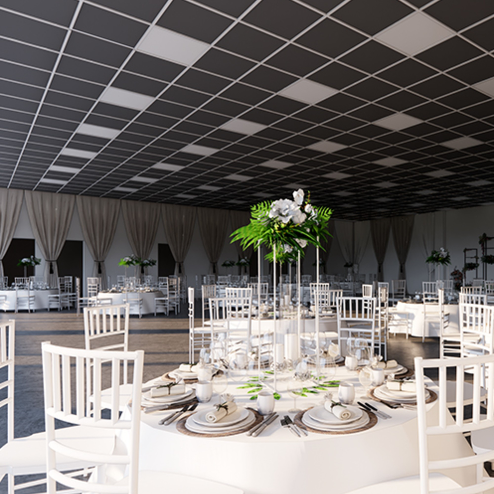 A large event hall with white round tables, chairs, and floral centerpieces under a checkered ceiling.