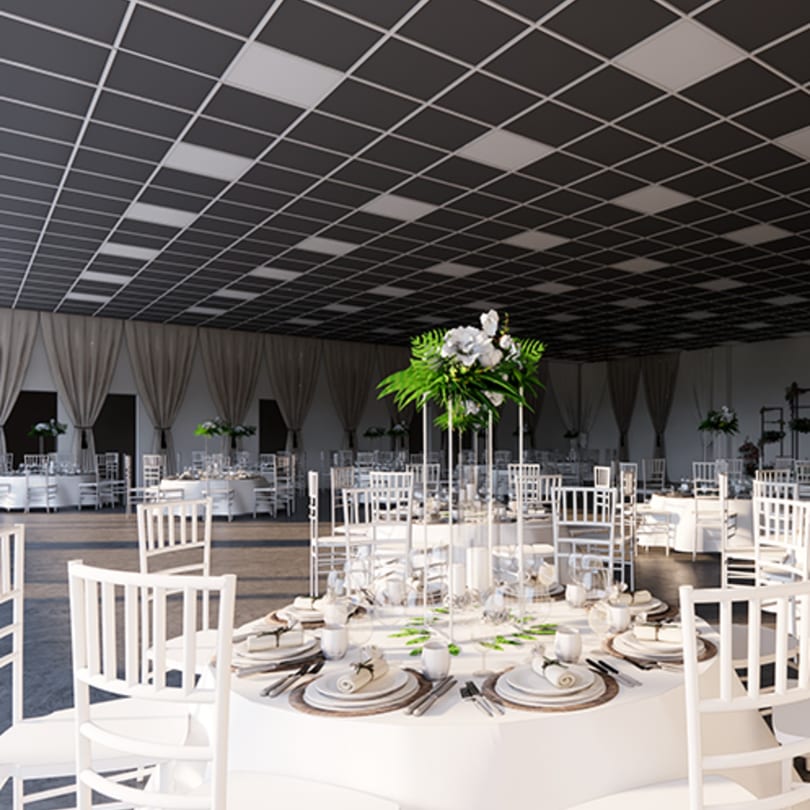 A large event hall with white round tables, chairs, and floral centerpieces under a checkered ceiling.