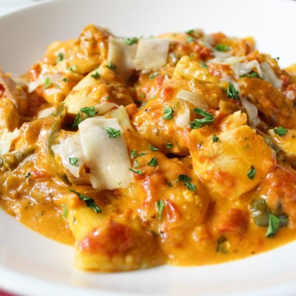 Close-up of Indian butter chicken, garnished with fresh herbs and cheese, in a white bowl.