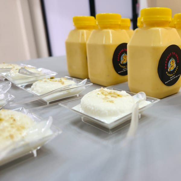 Mango lassi bottles and small dessert cups with white pudding and nuts on a table.