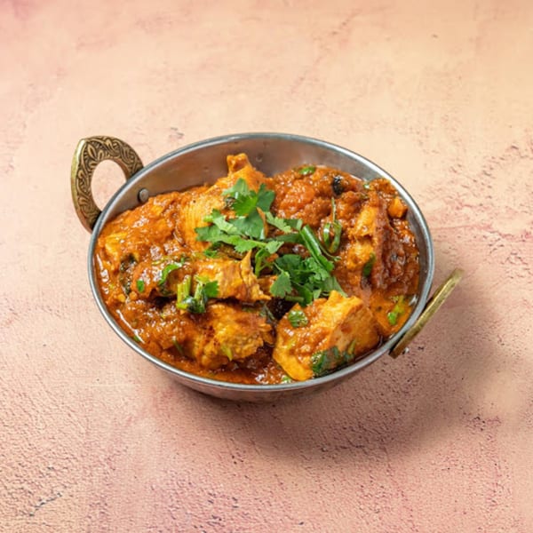 Passage To India's chicken curry, garnished with fresh cilantro, served in a traditional metal karahi.