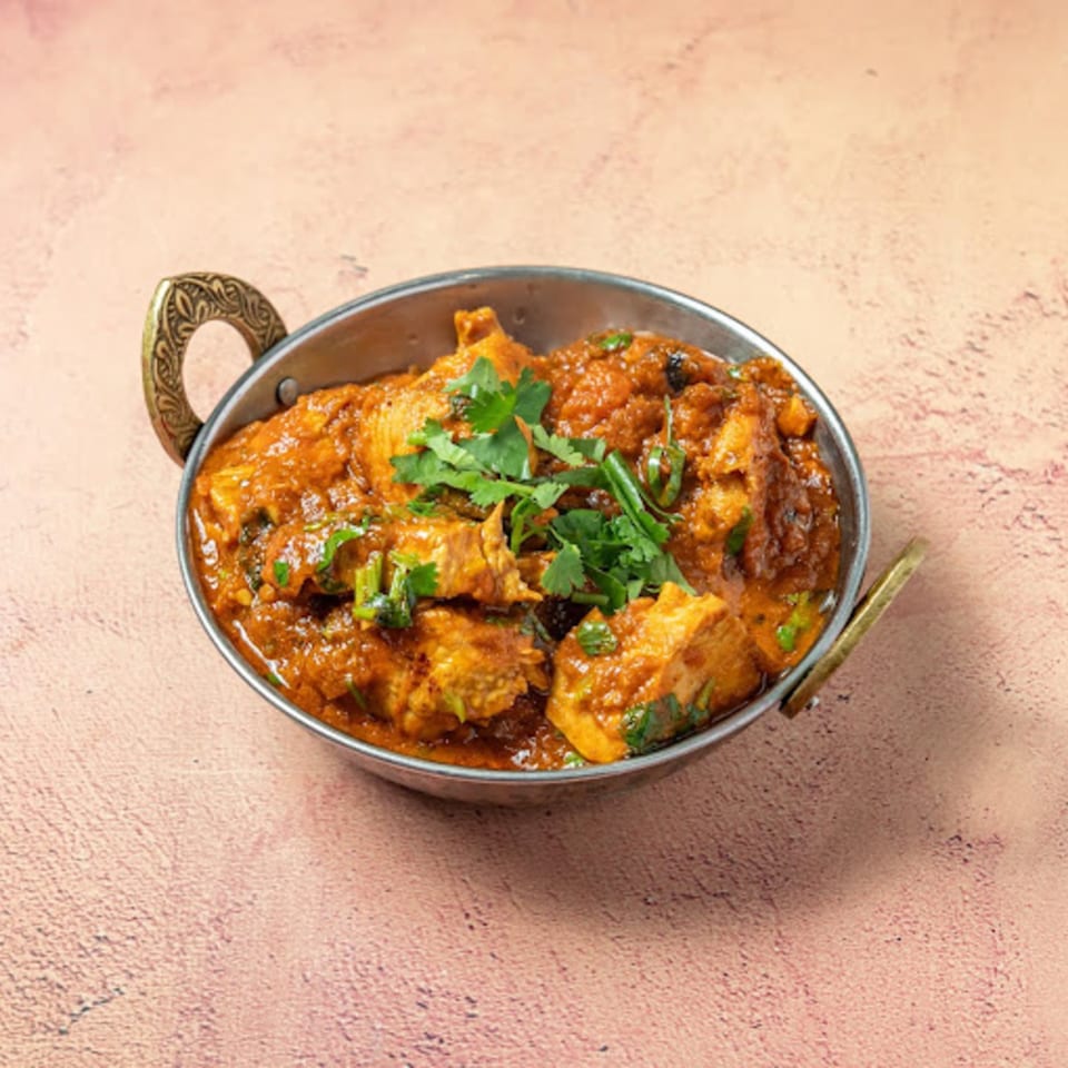 Passage To India's chicken curry, garnished with fresh cilantro, served in a traditional metal karahi.
