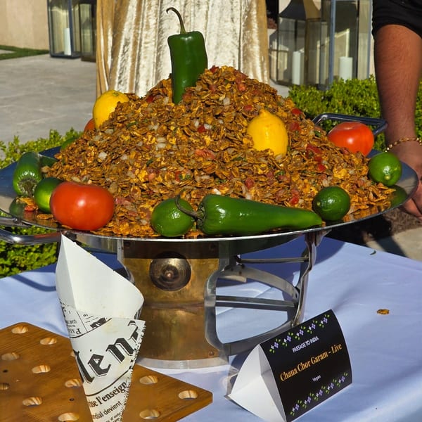 A large Chana Chor Garam dish, garnished with lemons, limes, tomatoes, and green peppers.