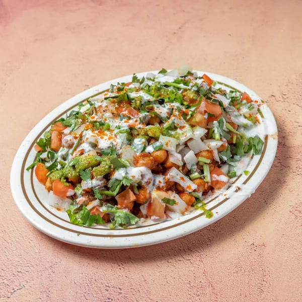 A vibrant Indian chaat dish with chickpeas, tomatoes, onions, cilantro, and sauces on a white plate.